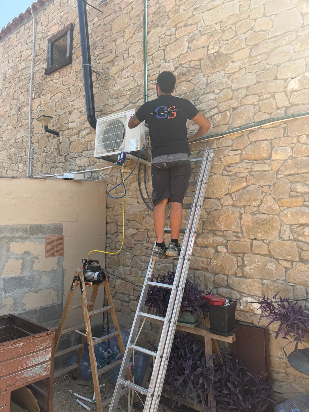 Técnico de Goodi Systems instalando un aire acondicionado en una fachada de piedra