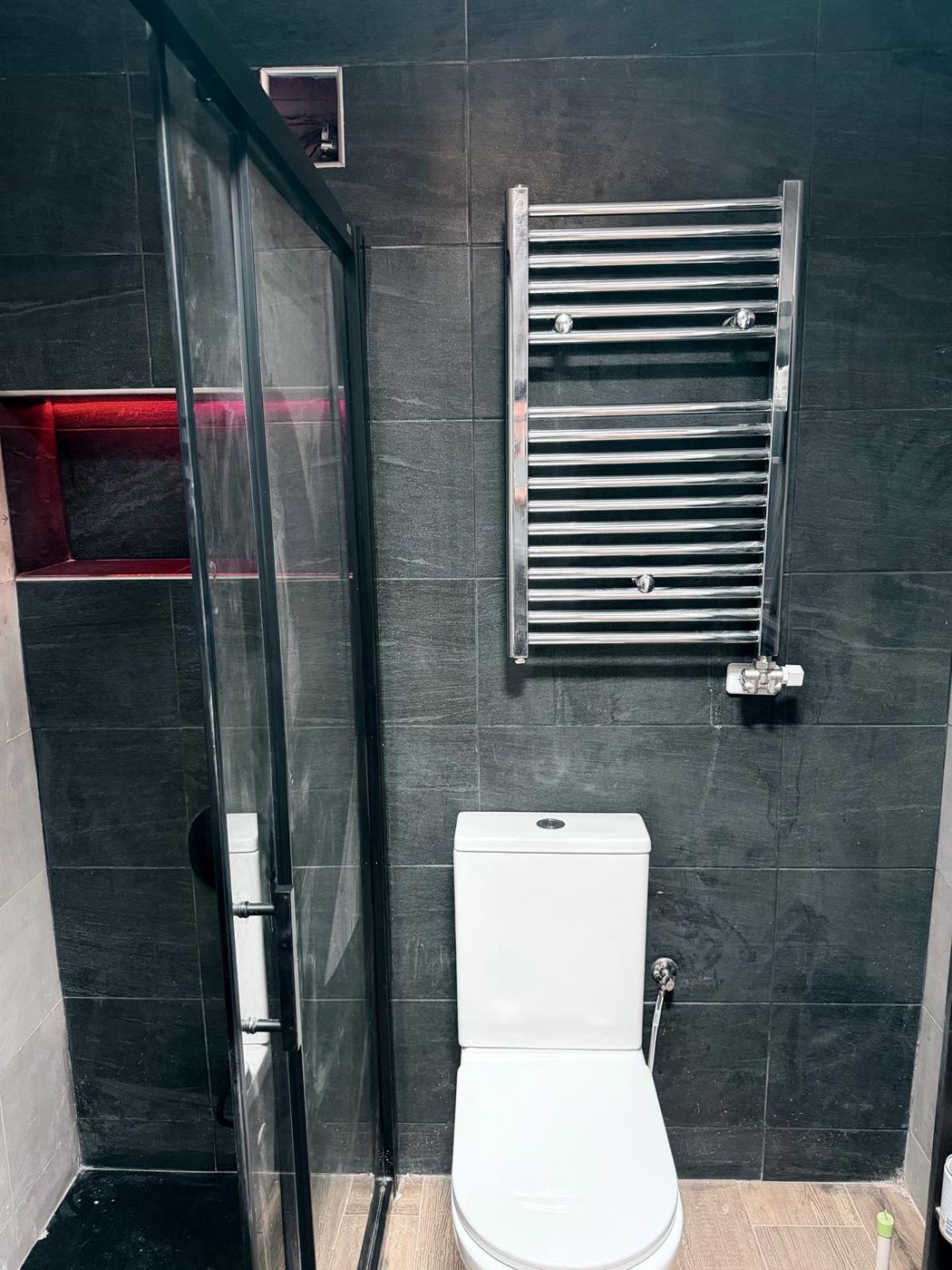 Baño con azulejo gris oscuro, mampara negra, toallero cromado y hornacina iluminada
